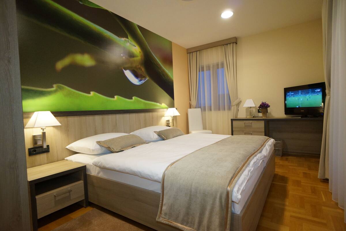 Una habitación de hotel con una cama grande, dos mesitas de noche con lámparas, un televisor y un mural en la pared.