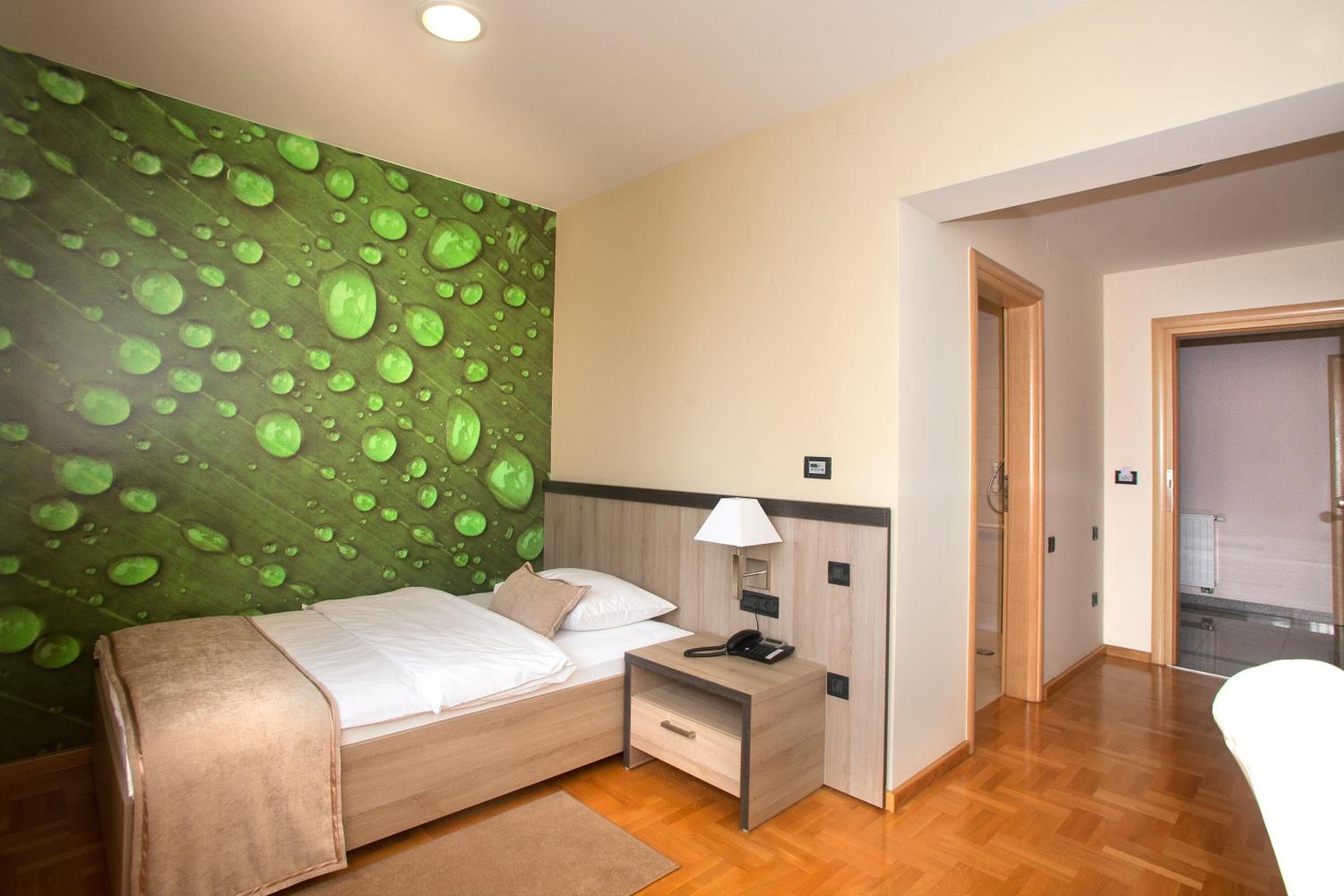 A hotel room with a bed, bedside table, lamp, and a wall with a green leaf pattern.