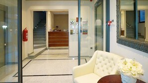 A hotel lobby with a white sofa, a reception desk, a staircase, and a fire extinguisher.