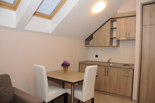 A modern kitchen with wooden cabinets, a white tiled backsplash, and a skylight above the dining area. - Hotel Calypso (Zagreb)