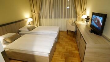 A hotel room with two beds, a TV, a desk with a lamp, and a chair.