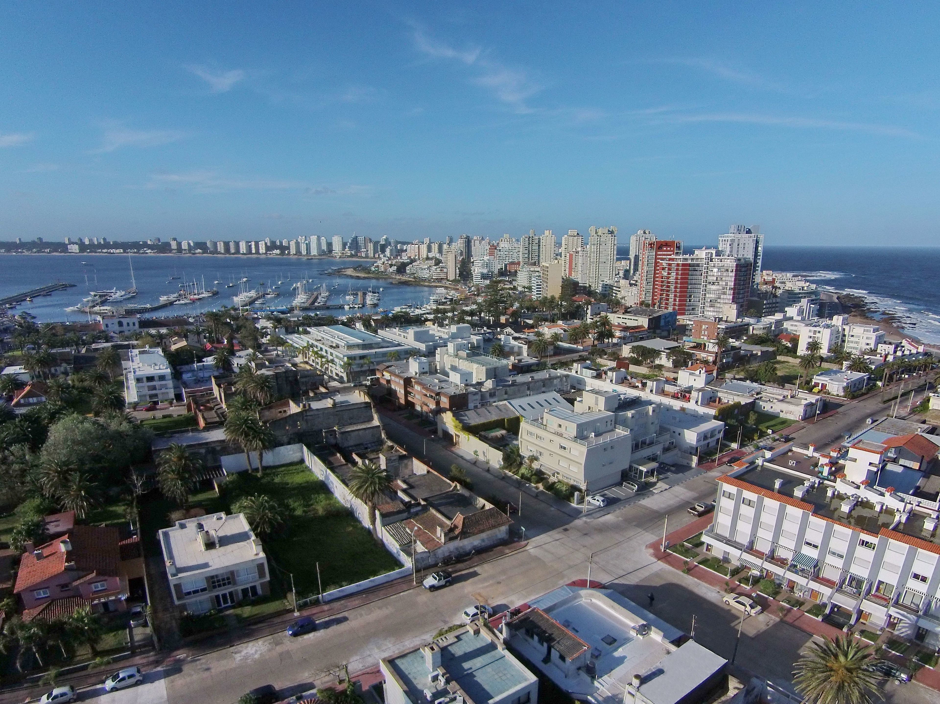 Un paisaje urbano costero con un puerto deportivo, edificios residenciales y un hotel moderno y alto.