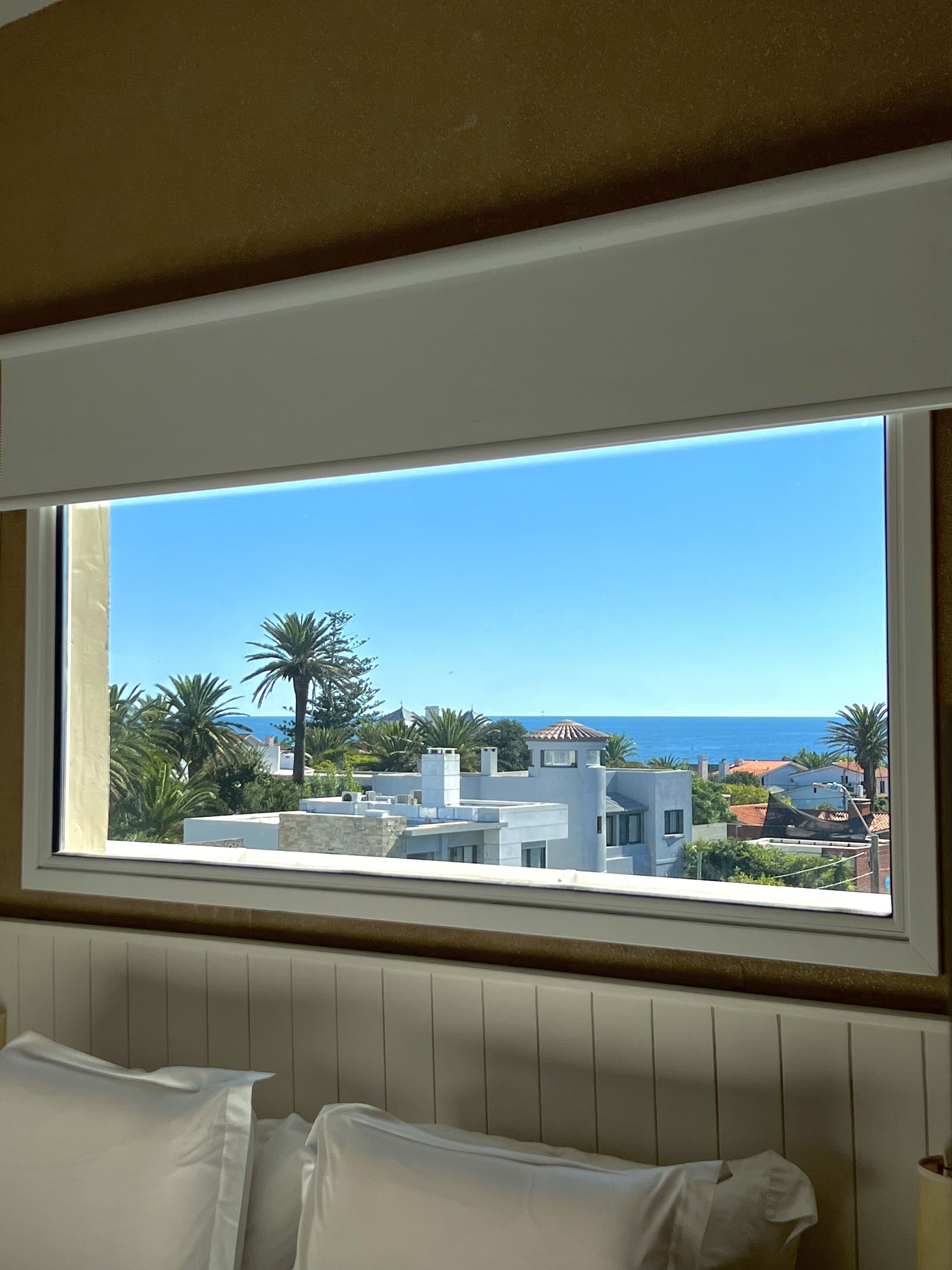 Una habitación con un ventanal grande que da a una zona costera con edificios y palmeras.