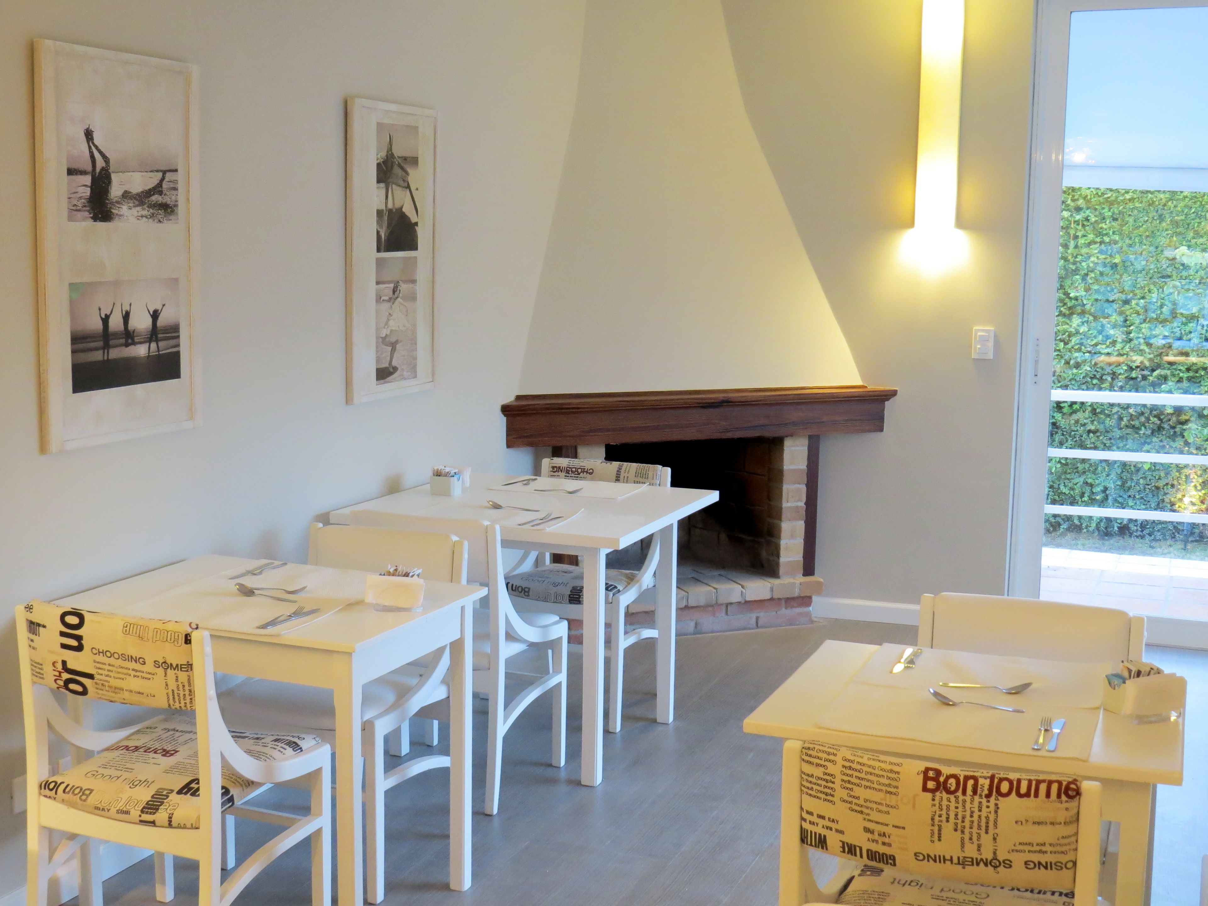 Un comedor con mesas y sillas blancas, una chimenea y cuadros en las paredes.