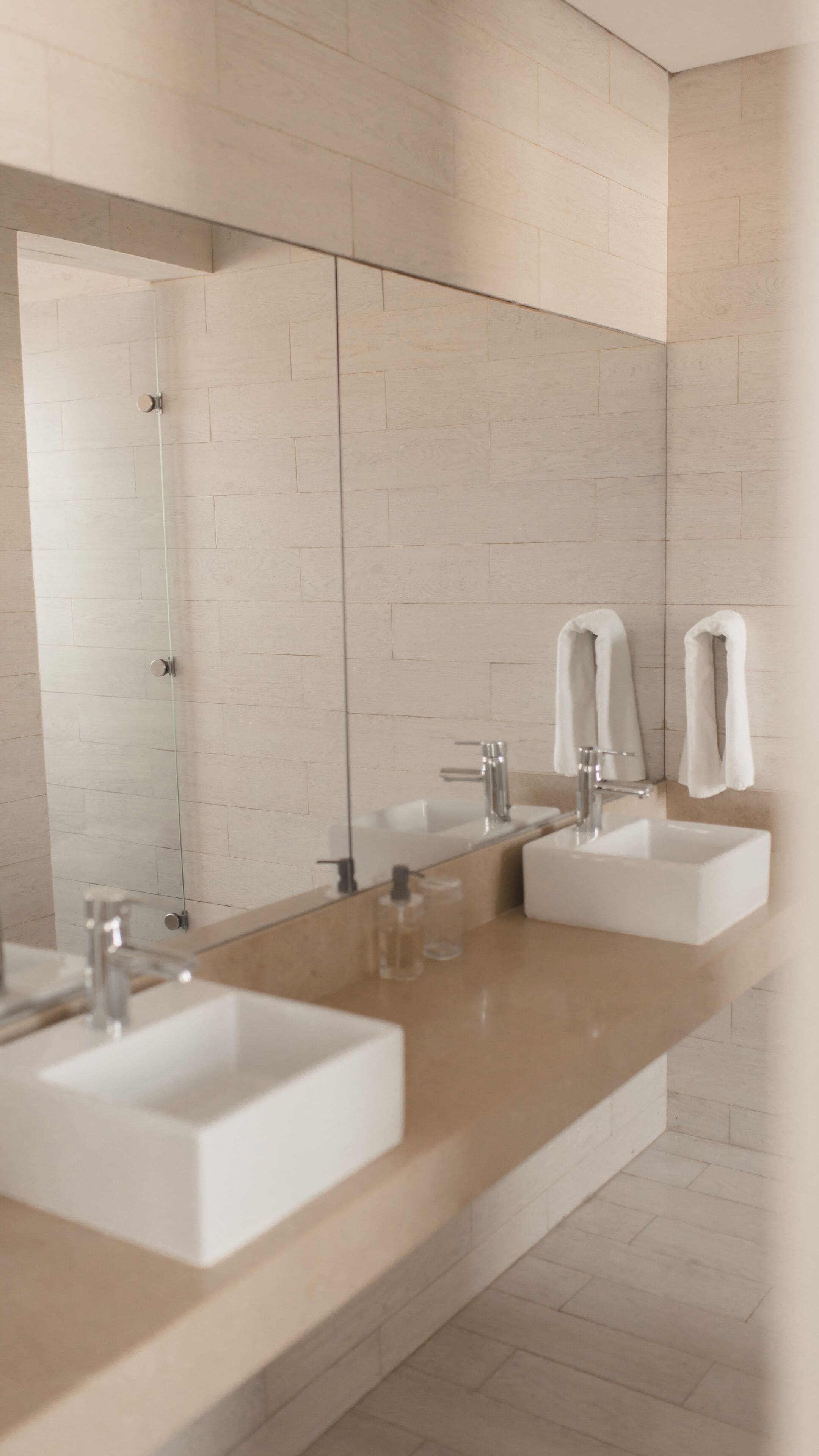 Een moderne badkamer met twee wasbakken, een grote spiegel en een handdoekdispenser.