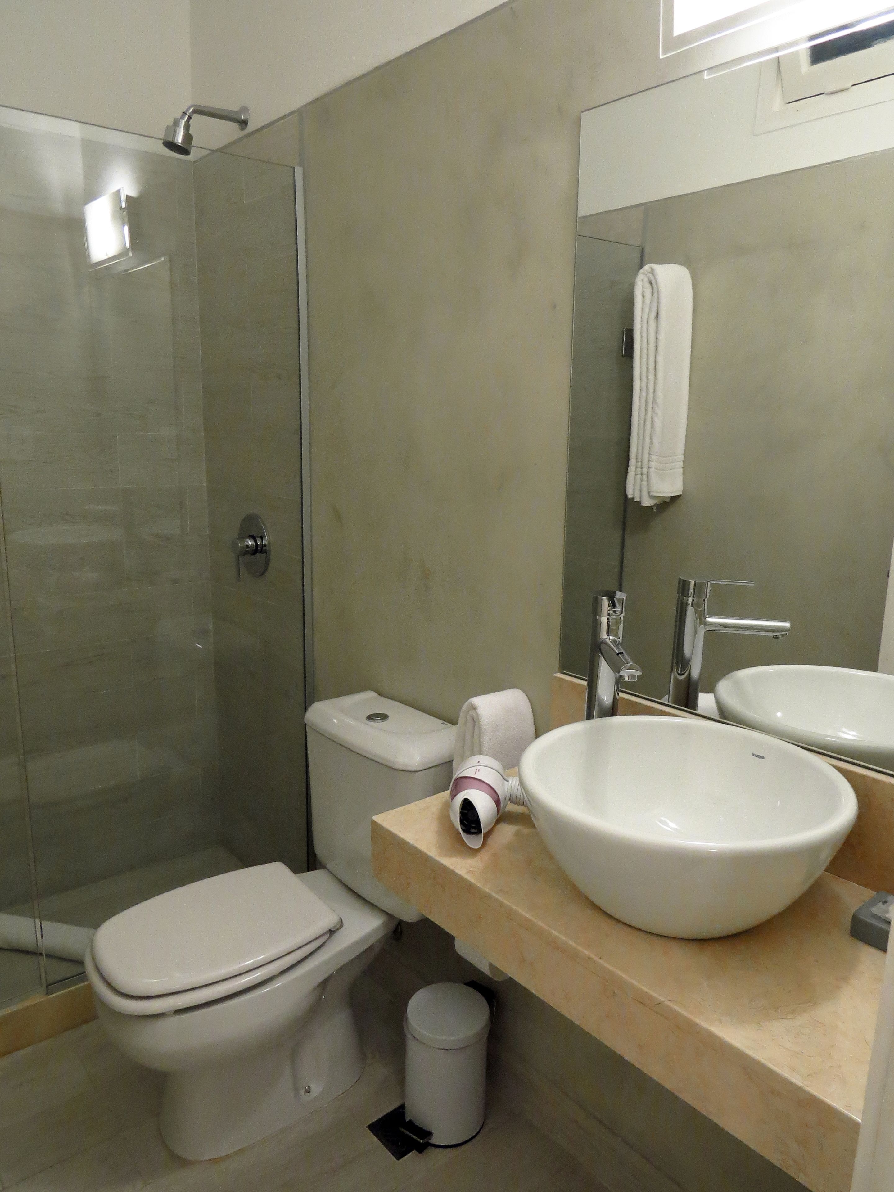 Un baño moderno con cabina de ducha de vidrio, inodoro, lavamanos y espejo.