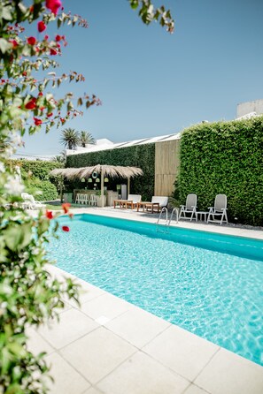 A swimming pool with lounge chairs and a bar area, surrounded by greenery and a clear sky. - Atlántico Boutique Hotel (Punta del Este)