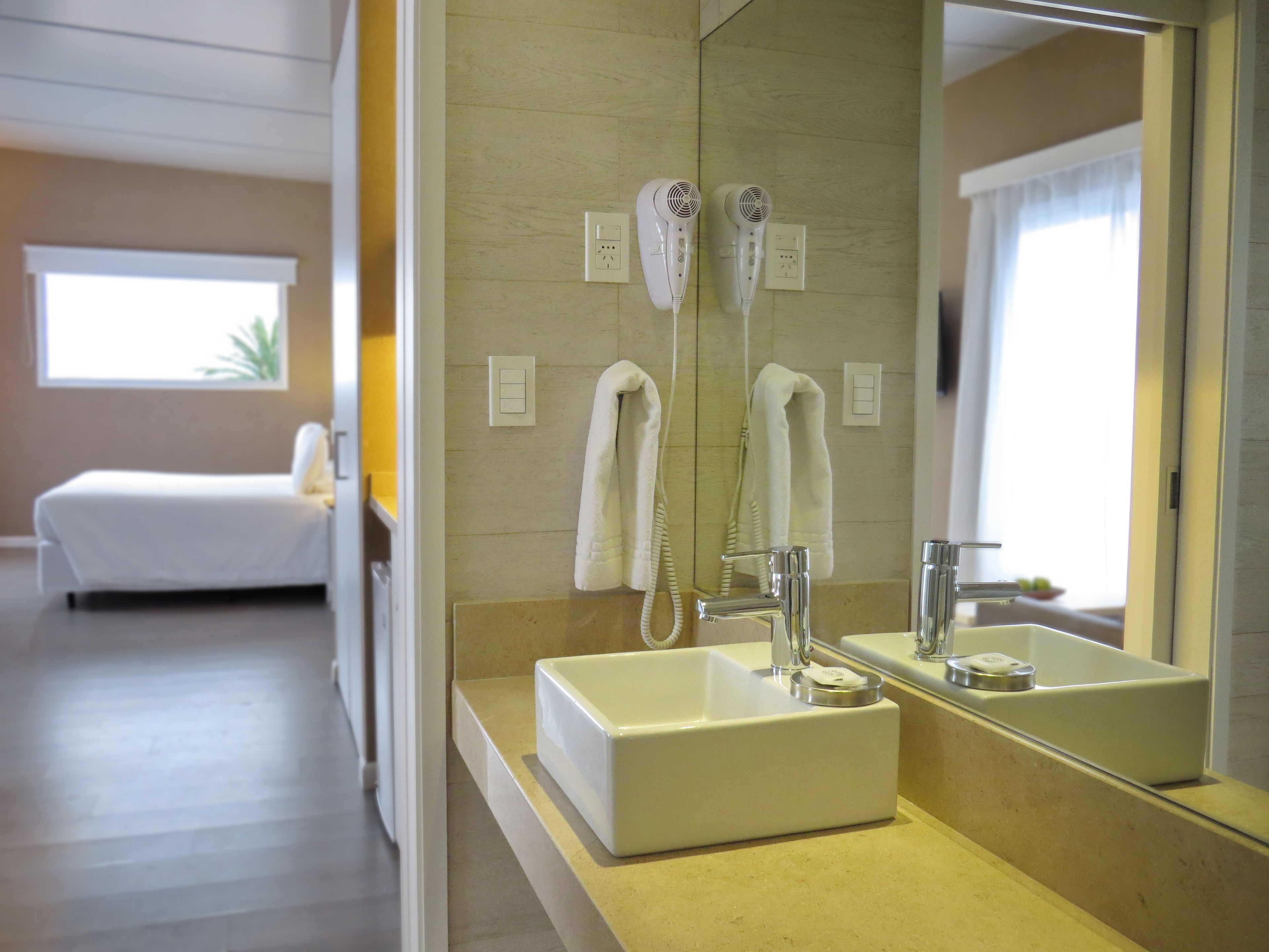 Un baño de hotel con un espejo grande, un lavamanos y dos secadores de pelo montados en la pared.