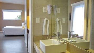 Un baño de hotel con un espejo grande, un lavamanos y dos secadores de pelo montados en la pared.