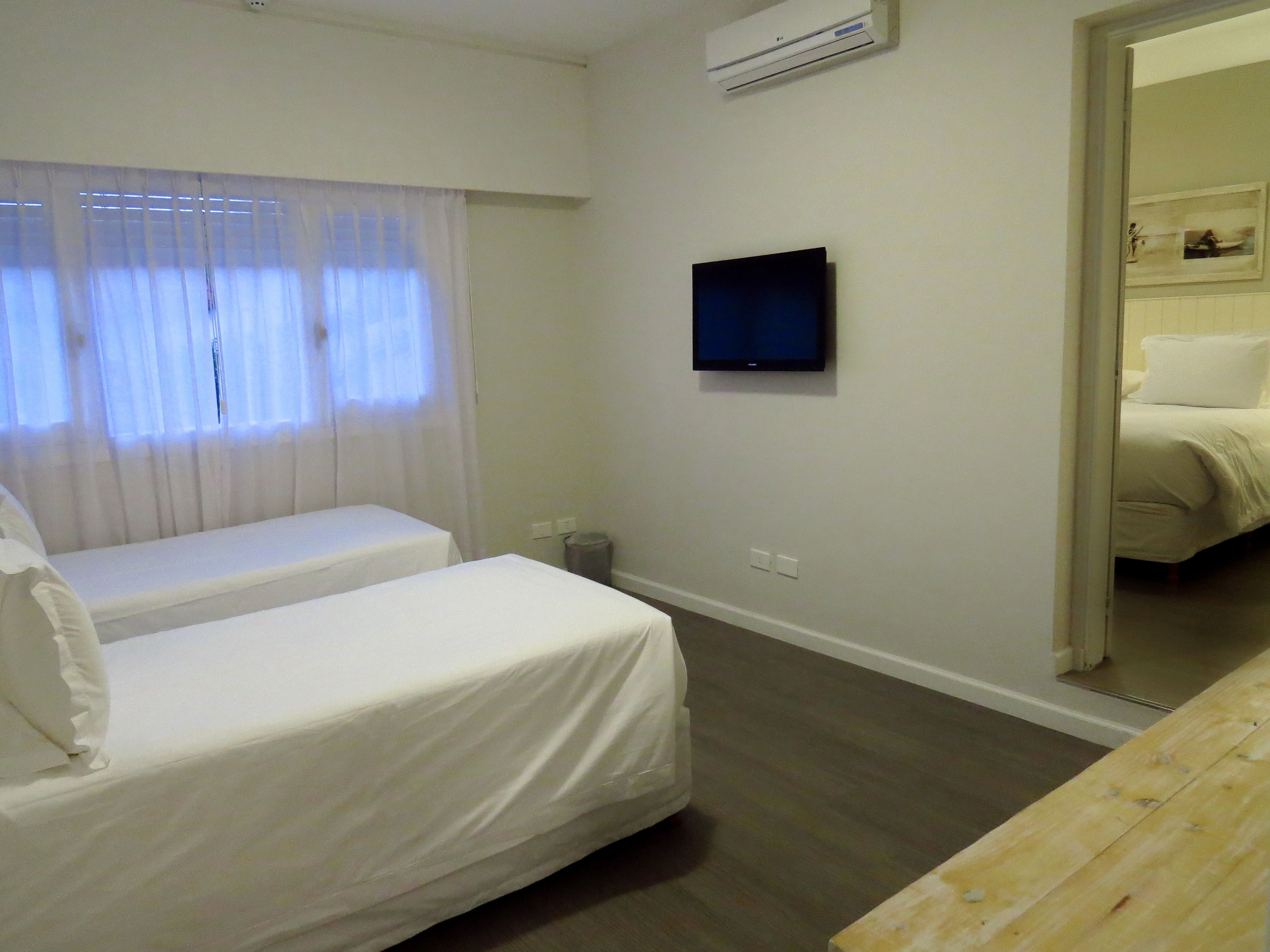 Ein Hotelzimmer mit zwei Einzelbetten, einem an der Wand montierten Fernseher und einer Klimaanlage.