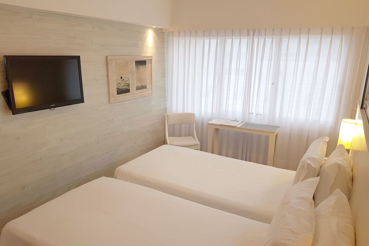 Une chambre d’hôtel avec deux lits, une télévision, une chaise, une petite table et une fenêtre avec des rideaux.