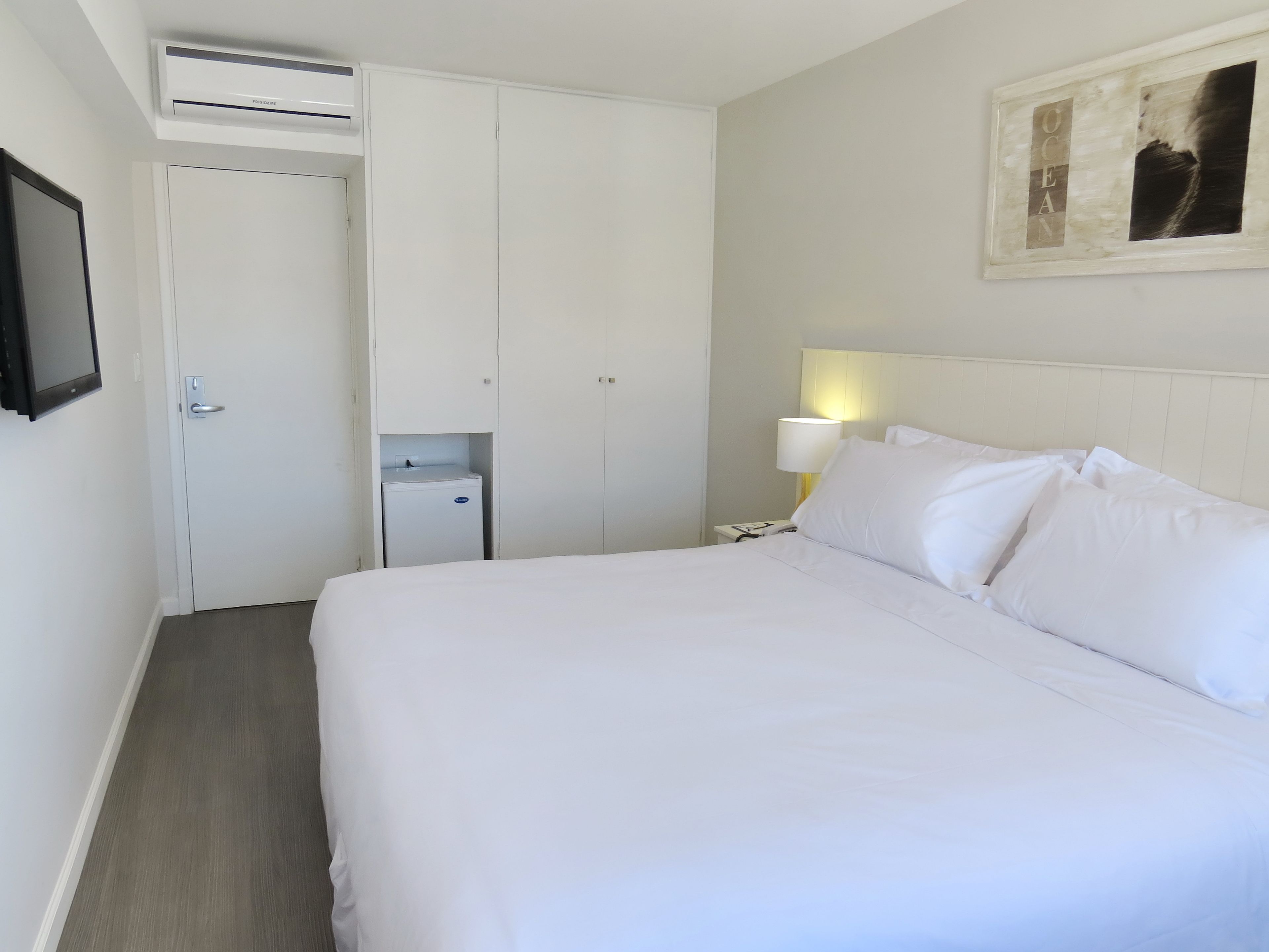 A hotel room with a bed, a nightstand, a lamp, a wardrobe, and an air conditioning unit.