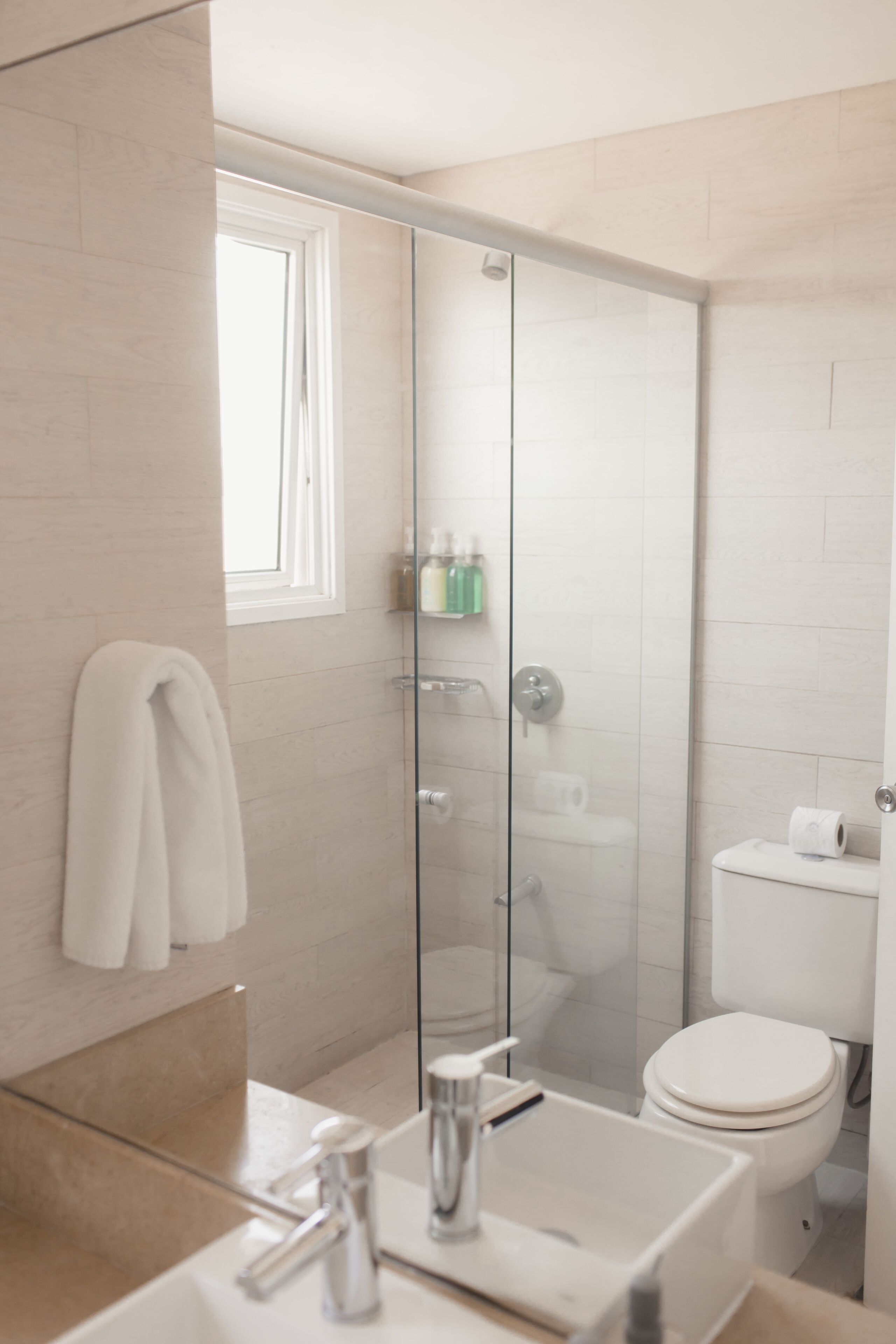 Un baño moderno con mampara de vidrio, un lavabo blanco y un inodoro.