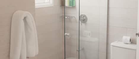 Un baño moderno con mampara de vidrio, un lavabo blanco y un inodoro.
