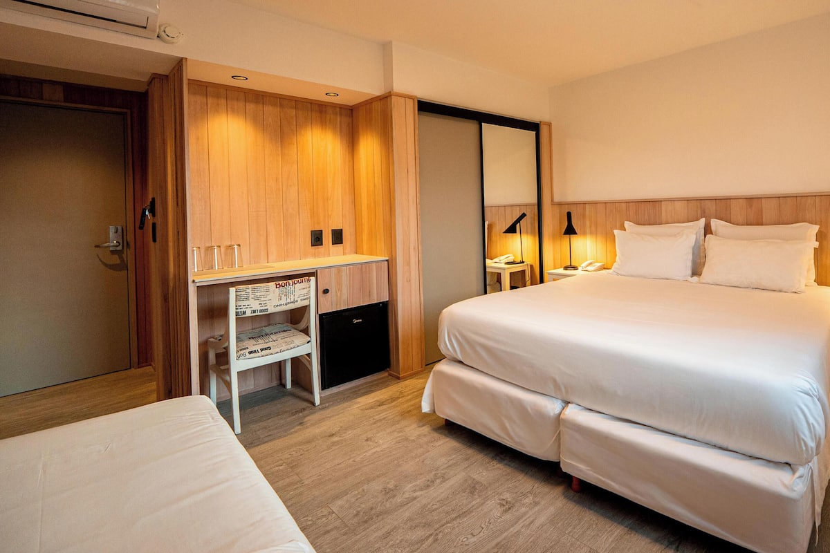Une chambre d’hôtel comprenant un lit, des tables de chevet, un bureau avec une chaise, une armoire et un miroir.