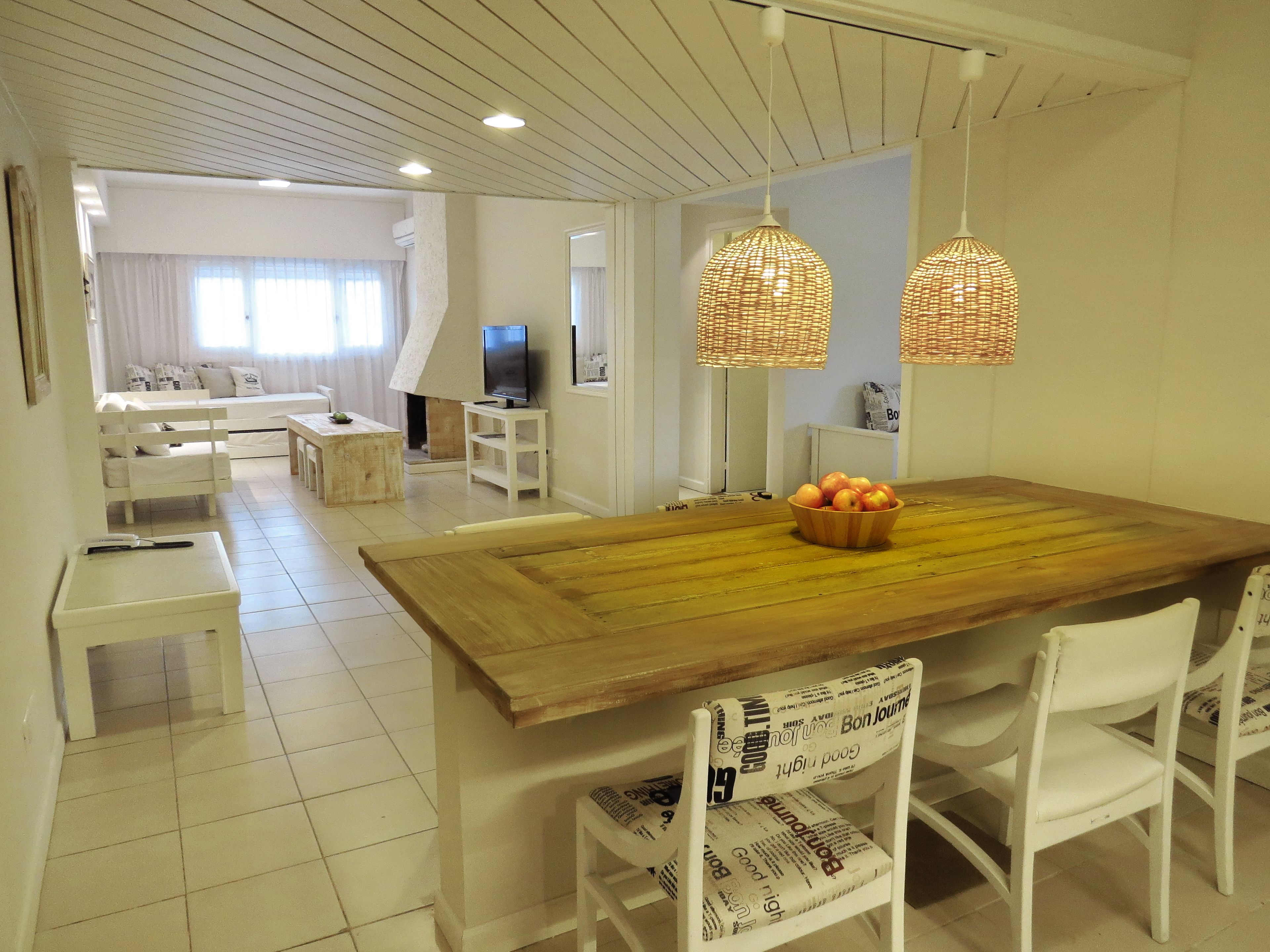 Una sala de estar moderna con una mesa de comedor de madera, sillas blancas y una televisión.