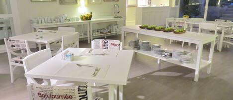 A dining area with white tables and chairs, a fruit bowl, and a sign with 'Bon Jour' on it.