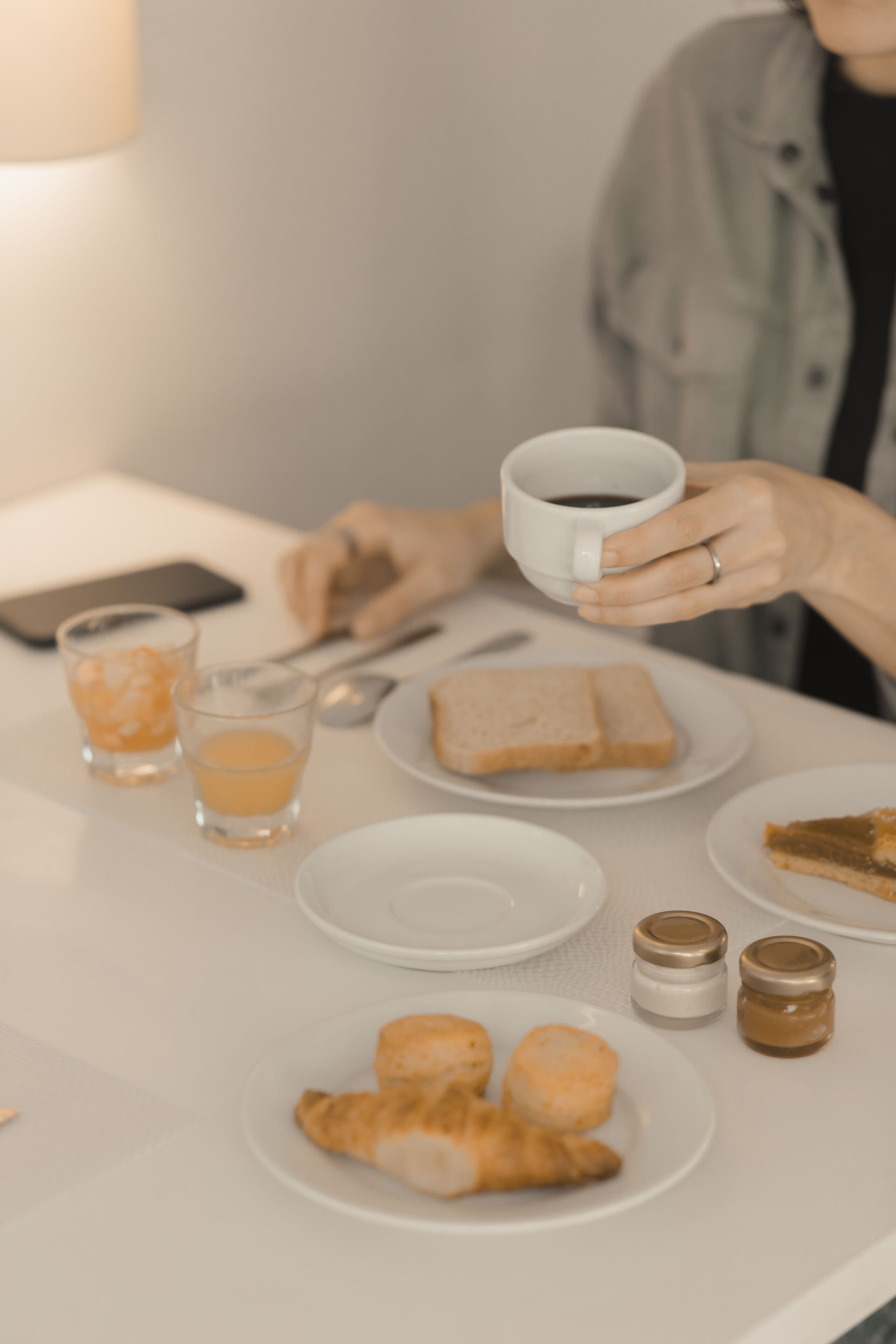 A table with a cup of coffee, a smartphone, glasses, and plates with food.