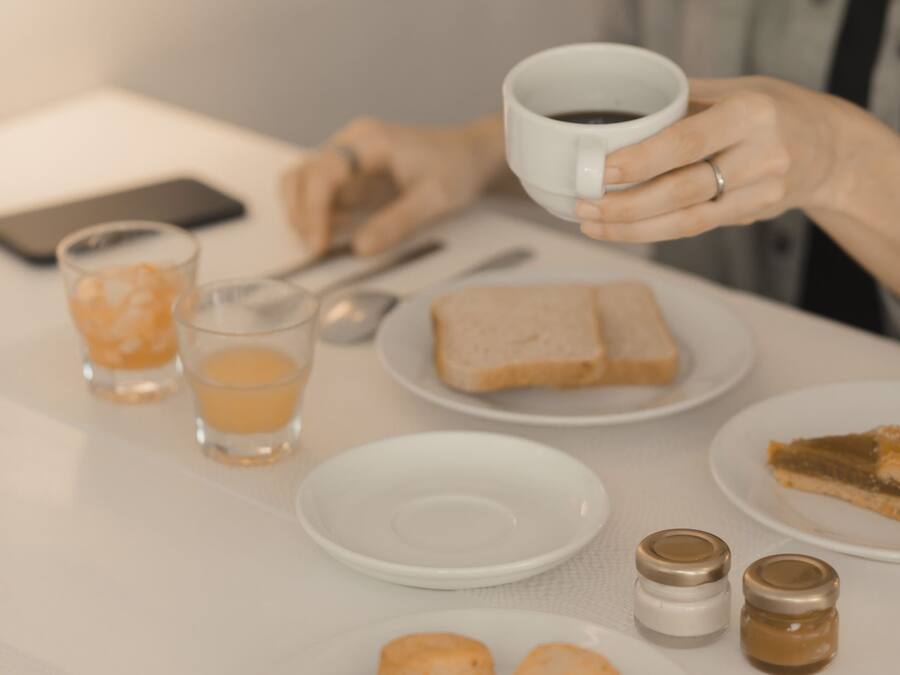 A table with a cup of coffee, a smartphone, glasses, and plates with food.