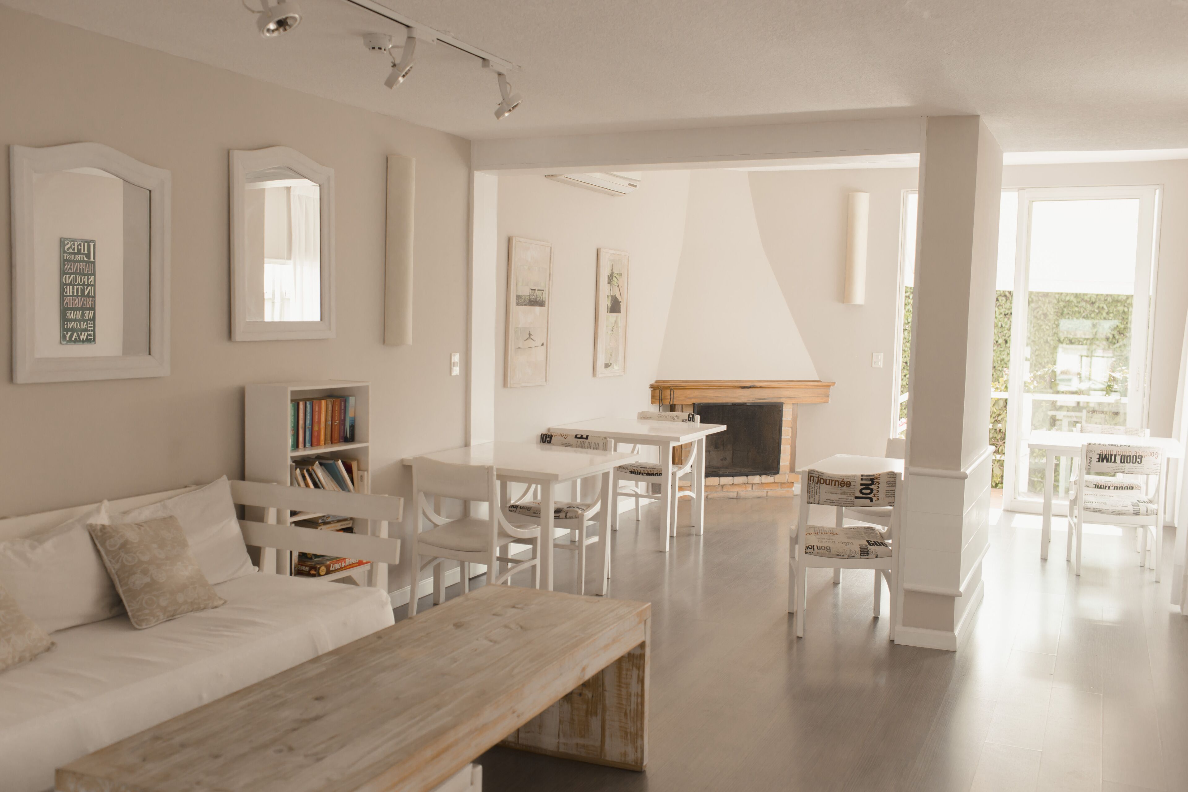 Una sala de estar moderna con un sofá blanco, una mesa de centro de madera y una chimenea. Hay sillas blancas y una mesa de comedor con libros.