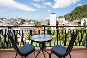 A balcony with two chairs and a table, overlooking a cityscape with buildings and greenery. - Casa Del M Phuket (Patong)