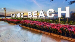 A sign reading "PATONG BEACH" with a view of the beach and a sunset in the background. - Casa Del M Phuket (Patong)
