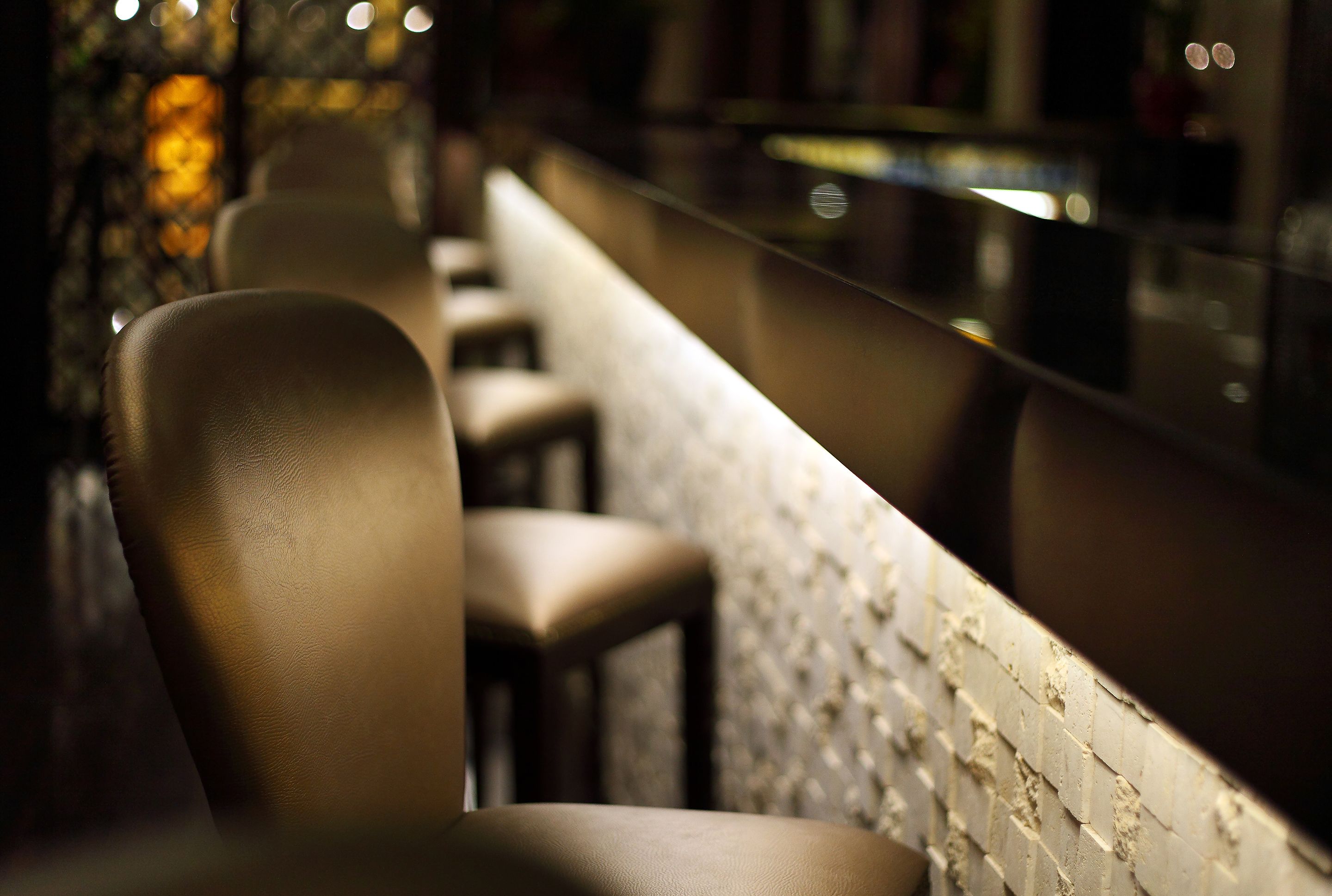 A row of bar stools with a textured wall behind them.