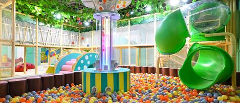Zona de juegos con piscina de pelotas, tobogán y estructura para escalar.