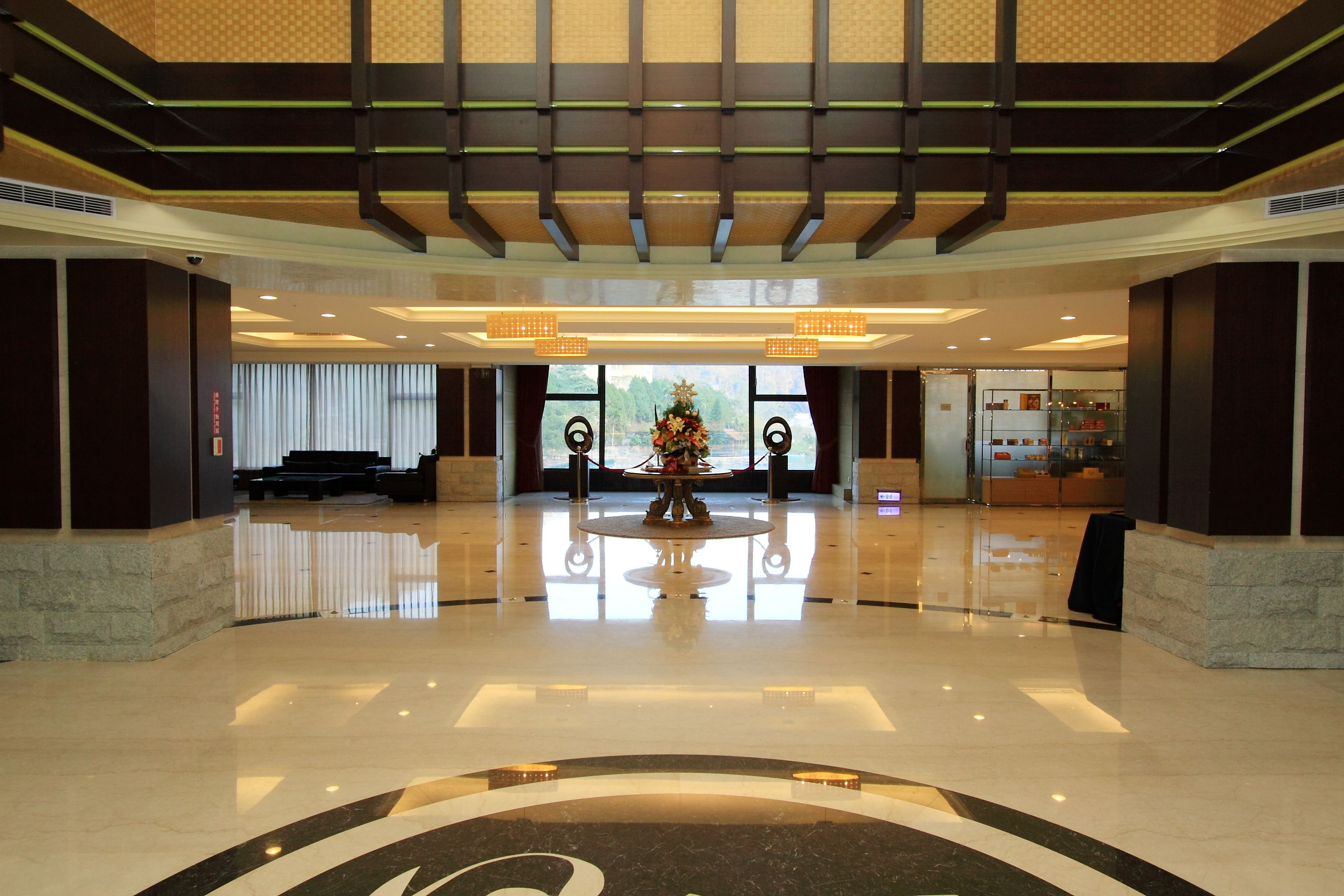 A spacious lobby with a polished floor, a central decorative table, and a reception area in the background.
