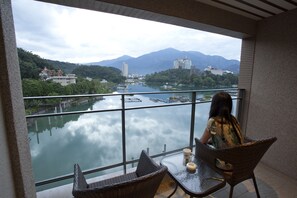 A balcony with wicker chairs and a table, overlooking a river with boats and buildings in the background. - Sun Moon Lake Hotel (Yuchi)