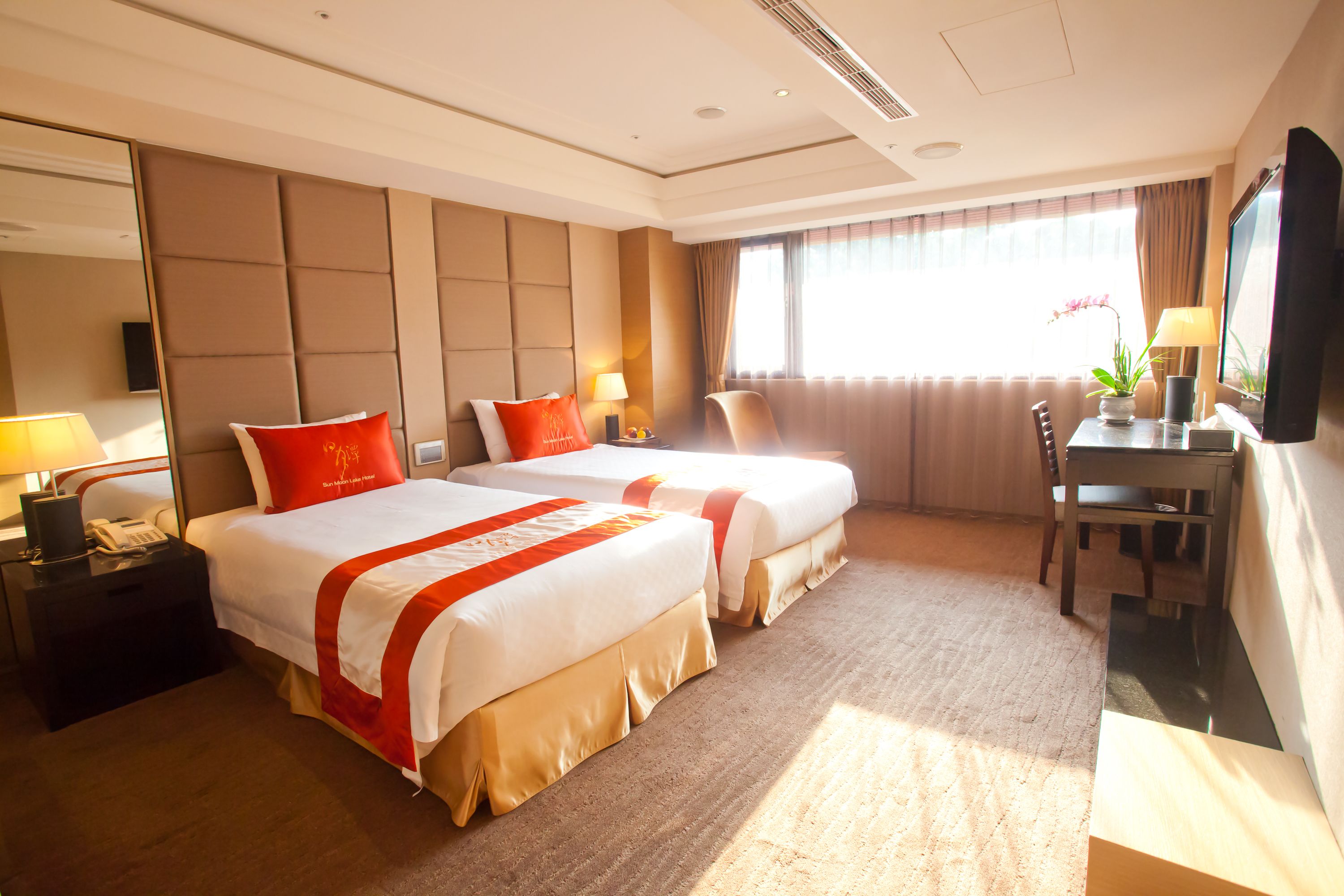 Une chambre d’hôtel avec deux lits, un bureau, une chaise, une télévision et une fenêtre avec des rideaux.