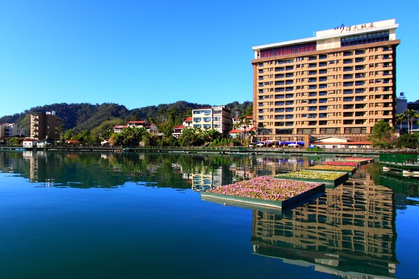 A hotel with a large building and a calm lake with flower arrangements in the foreground. - Sun Moon Lake Hotel (Yuchi)