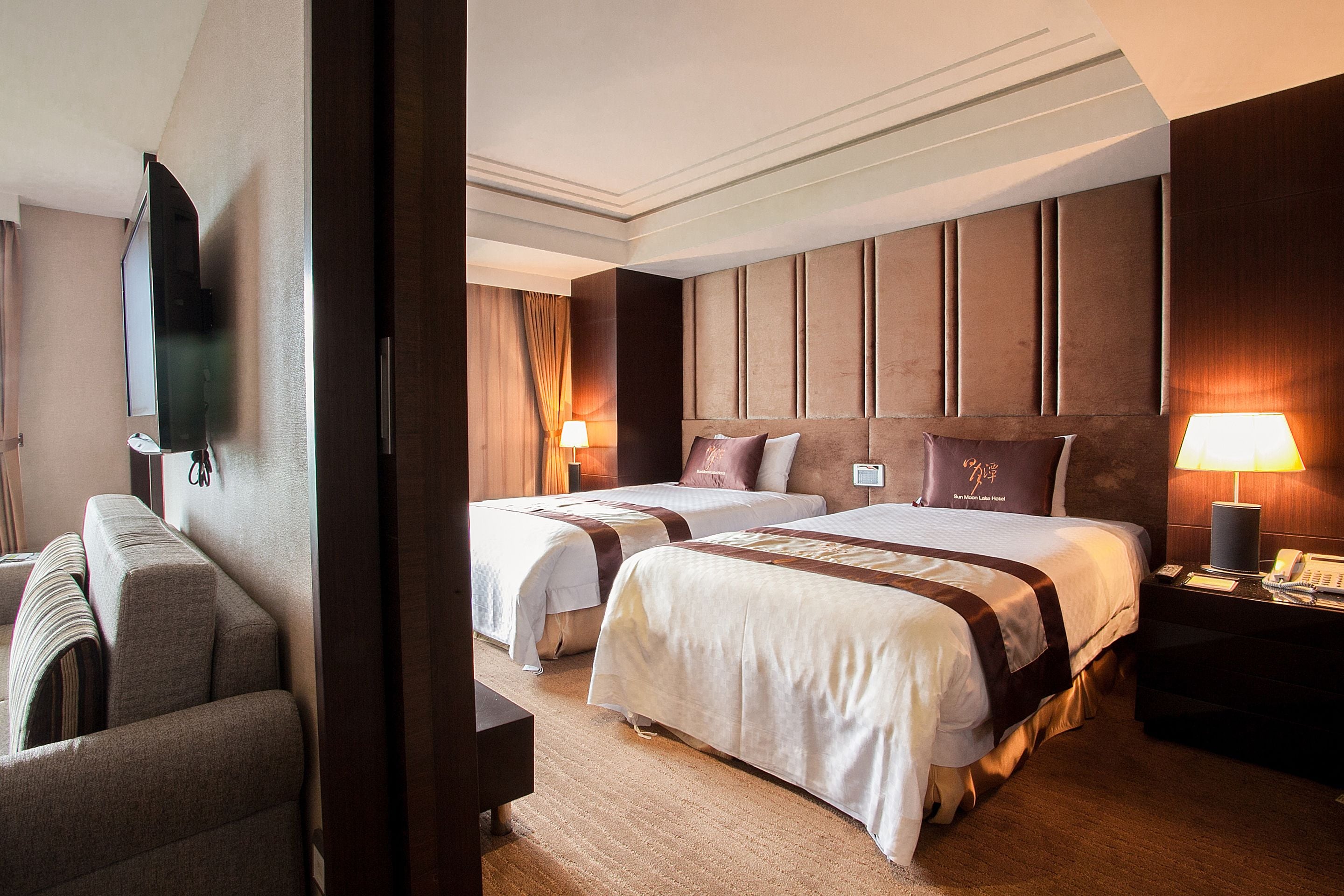 A hotel room with two beds, a sofa, a TV, and a lamp.