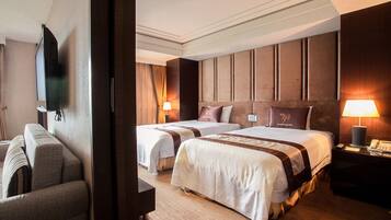 A hotel room with two beds, a sofa, a TV, and a lamp.