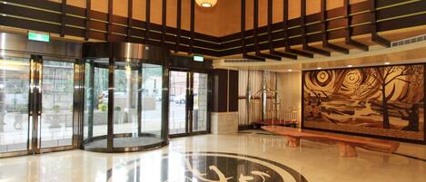A lobby with a circular floor design, glass revolving doors, and a large abstract mural.