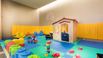 Un espace de jeux avec des blocs de mousse colorés, un train jouet et une petite maison de jeu.