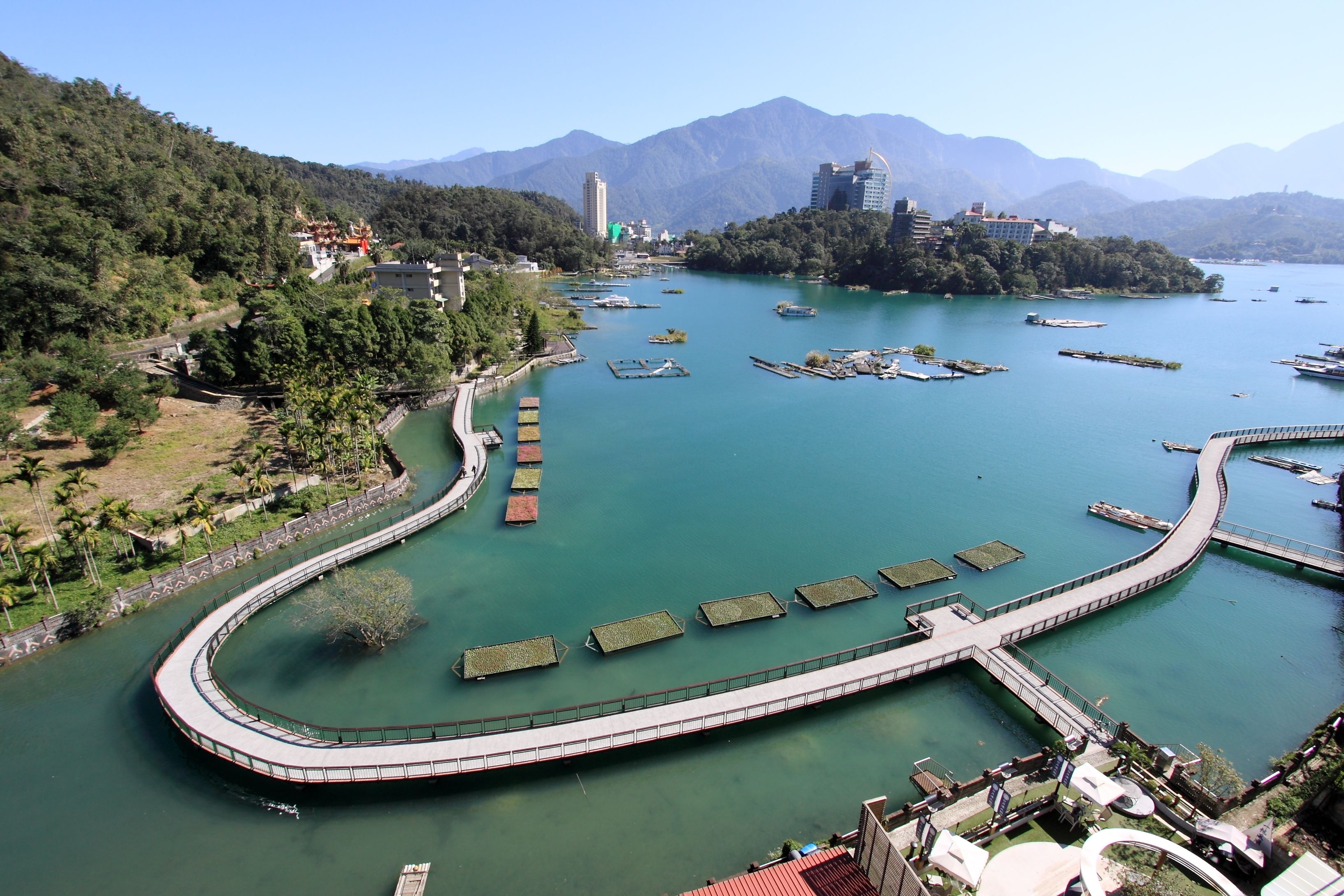 A waterfront area with a curved walkway, boats, and a mountainous backdrop.