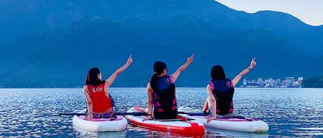 Tres personas en tablas de remo en un cuerpo de agua tranquilo, con montañas al fondo.