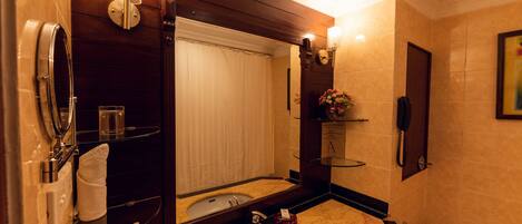 Un baño con lavamanos de mármol, un espejo, toallero, cabina de ducha de cristal, inodoro y un teléfono fijado en la pared.