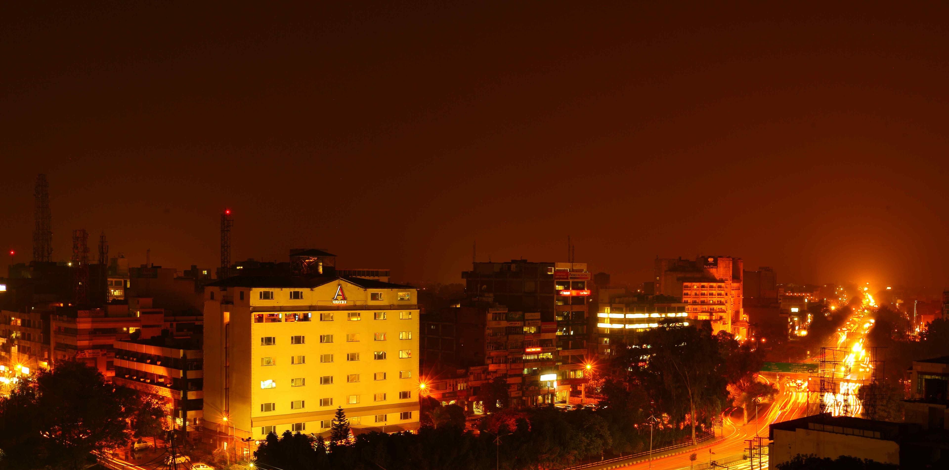 Un hotel de varios pisos con un llamativo logo 'A' en la fachada, rodeado de otros edificios y calles animadas por la noche.