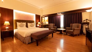 Une chambre d’hôtel avec un grand lit, deux fauteuils, une petite table et un ventilateur de plafond.