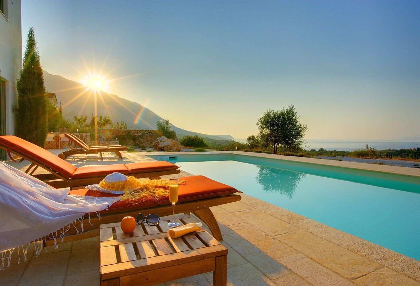 A poolside area with lounge chairs, a table with a drink, and a mountain view.