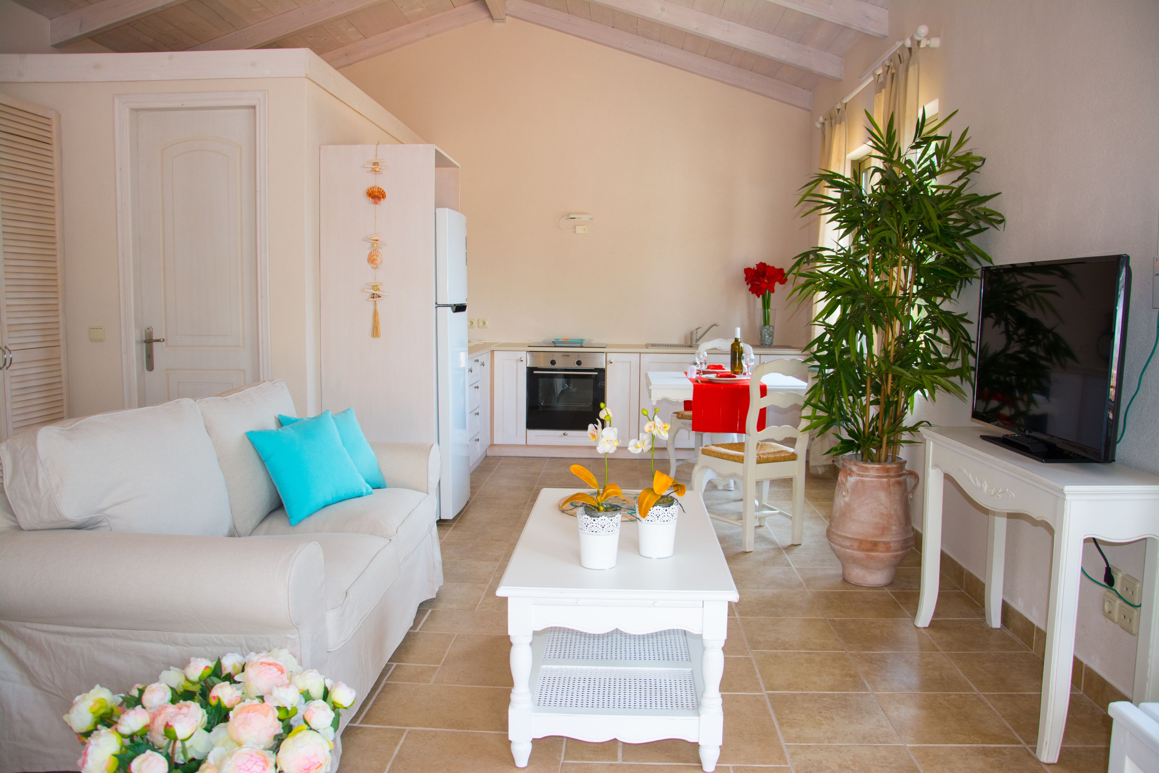 A living room with a white sofa, a coffee table, a TV, and a kitchen in the background.