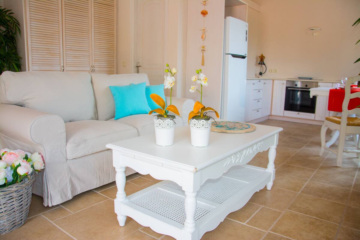 A living room with a white sofa, a coffee table, and a kitchen area with a refrigerator and oven.