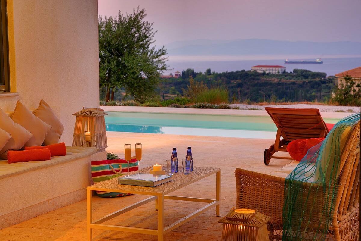 A cozy outdoor seating area with a pool view, a wicker chair, and a table with drinks and a book.