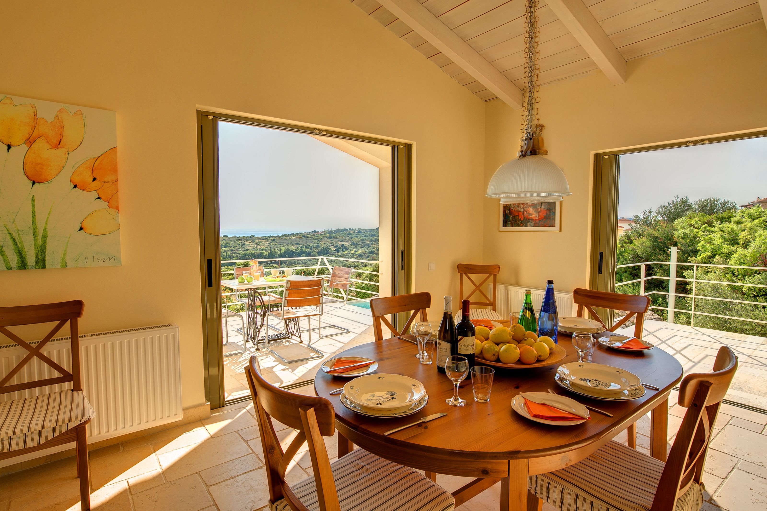 A dining area with a table set for four, chairs, a view of the outdoors, and a painting on the wall.