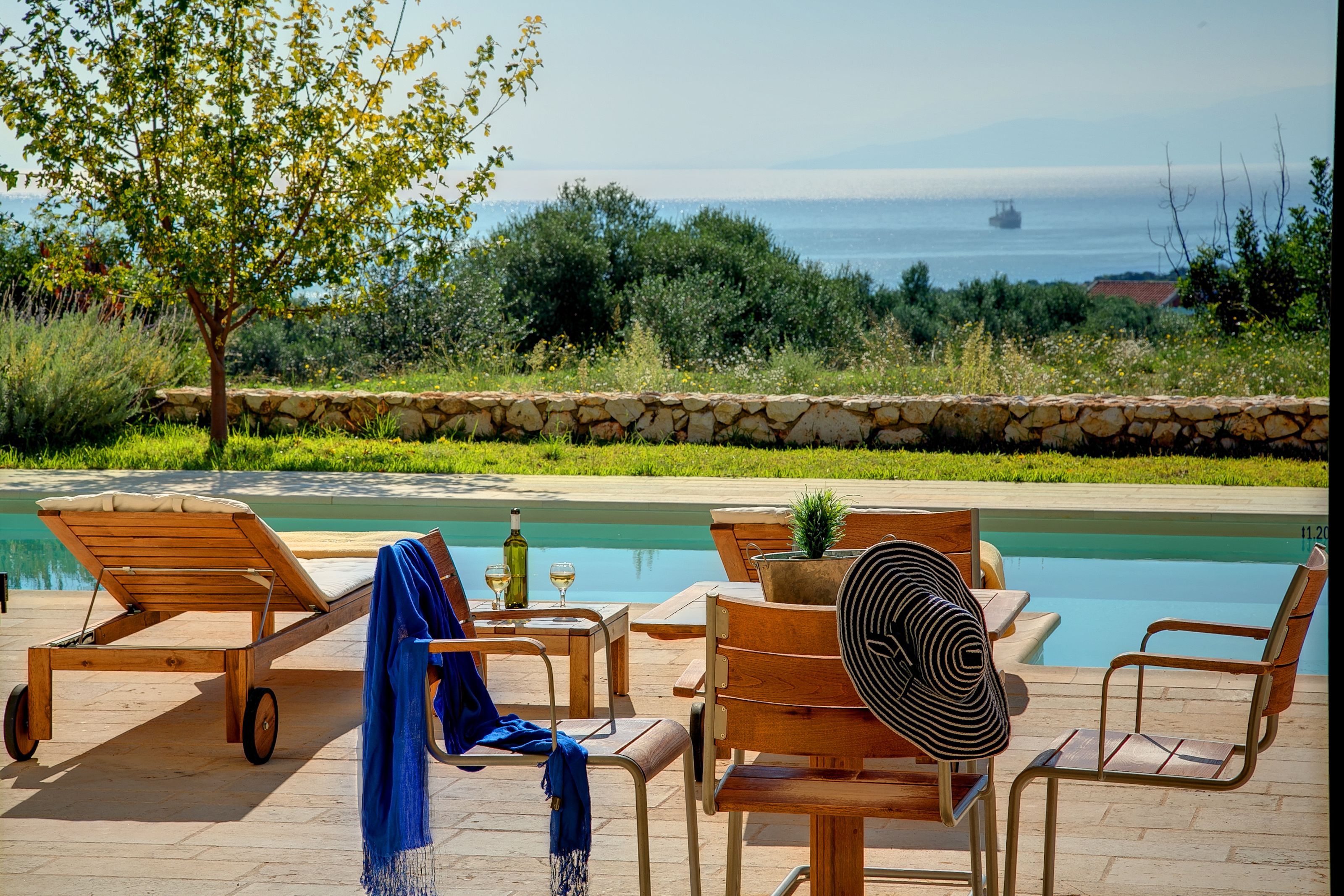 Un espace aménagé au bord de la piscine, avec des chaises longues, une table et une bouteille de vin.