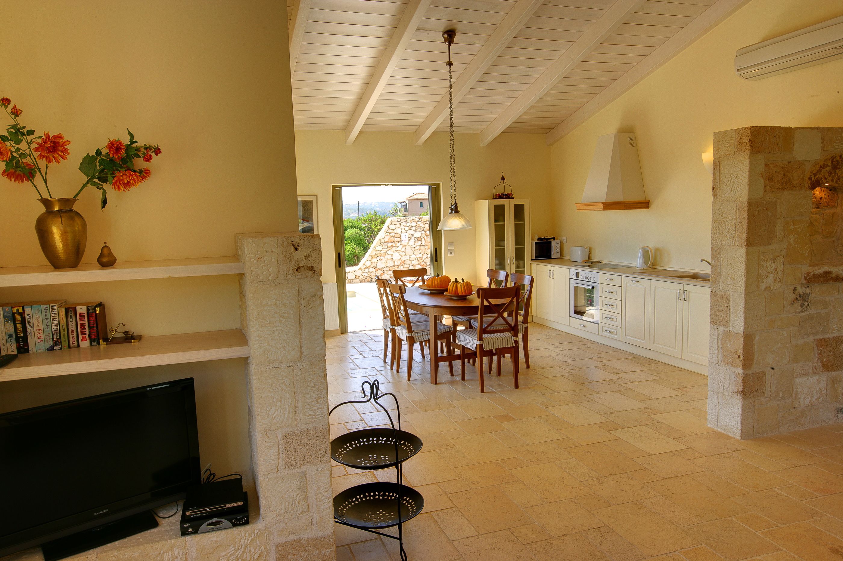A spacious kitchen with a dining area, stone fireplace, and a television on a shelf.