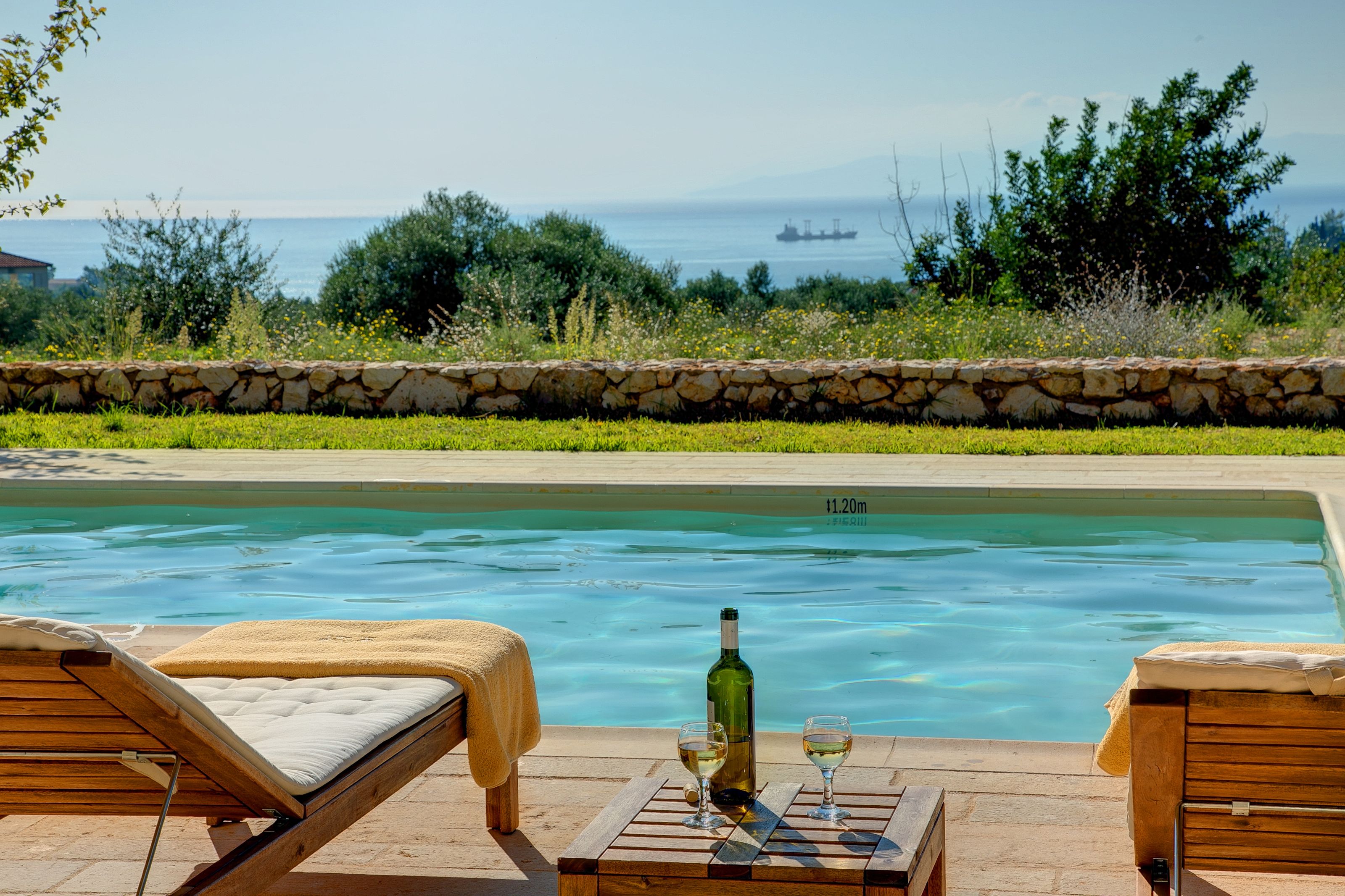 Zona junto a la piscina con sillones de descanso y una mesa con una botella y vasos.