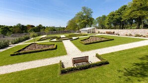 A landscaped garden with a central pathway, a bench, and a building with a stone wall. - Balmule House (Dunfermline)